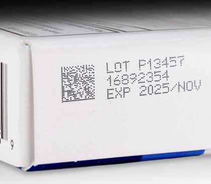 CIJ product marking: 2D code followed by three-line alpha-numeric text in black ink on coated paperboard